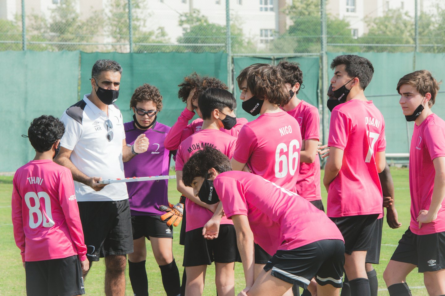 Entrenador de fútbol explica estrategia a jugadores adolescentes en un campo de césped.