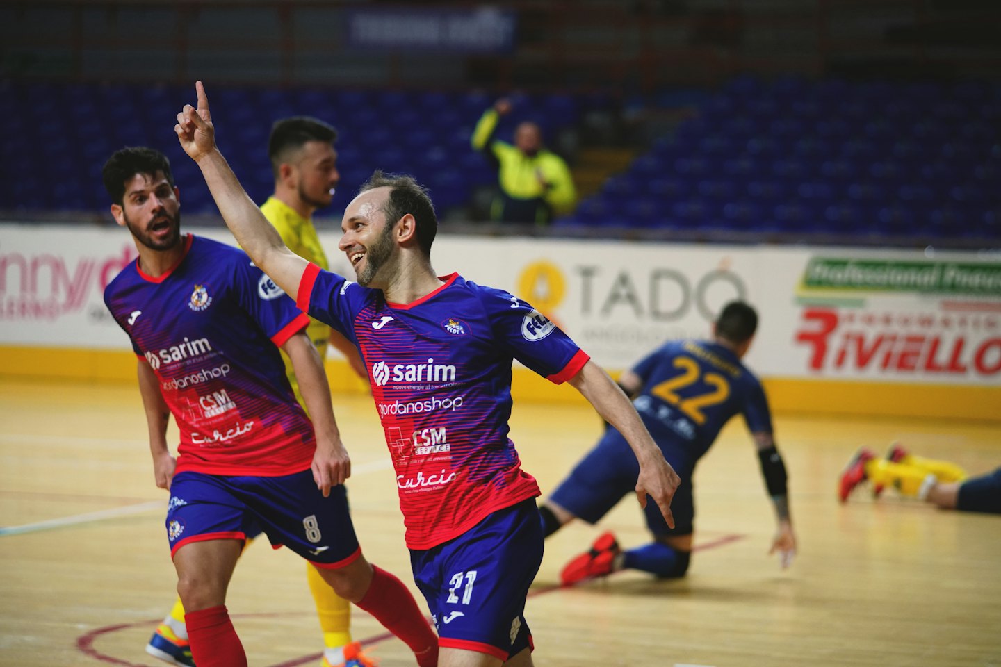 Dos jugadores de fútbol sala uniformados celebran una victoria en una cancha cubierta.