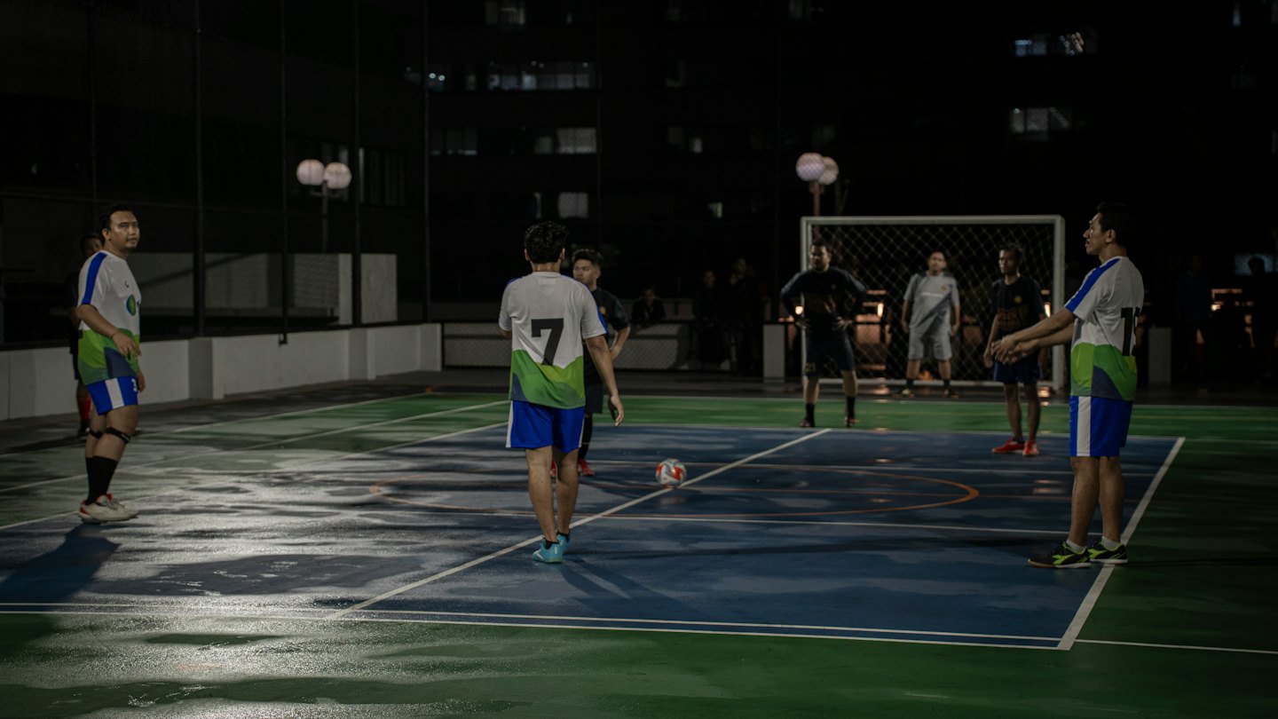 Hombres con camisetas juegan un partido de fútbol sala en una cancha mojada.