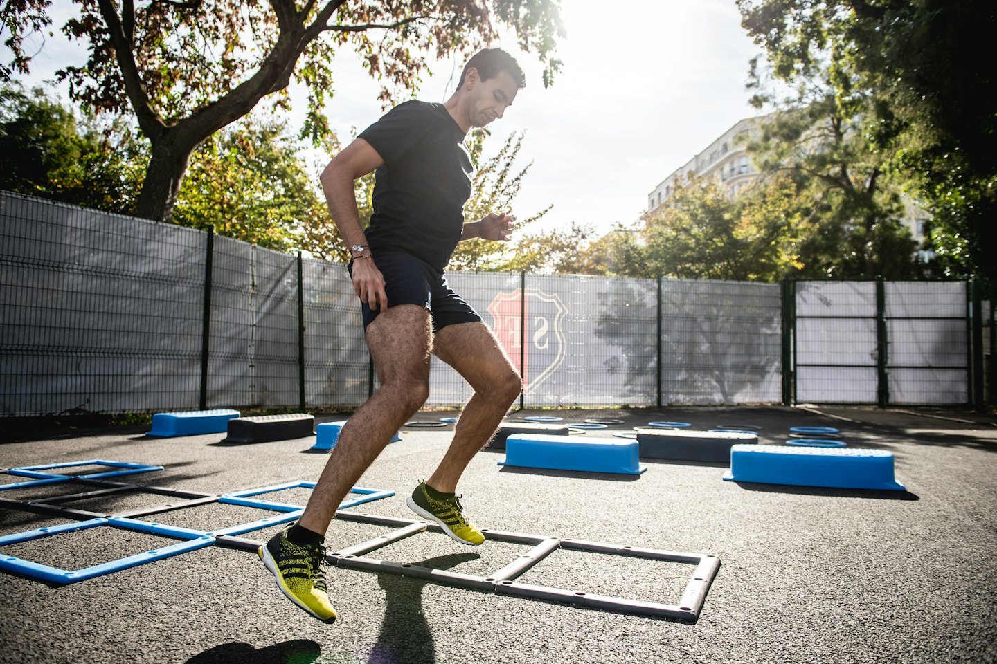 Hombre haciendo ejercicios de escalera de agilidad al aire libre en una cancha soleada.
