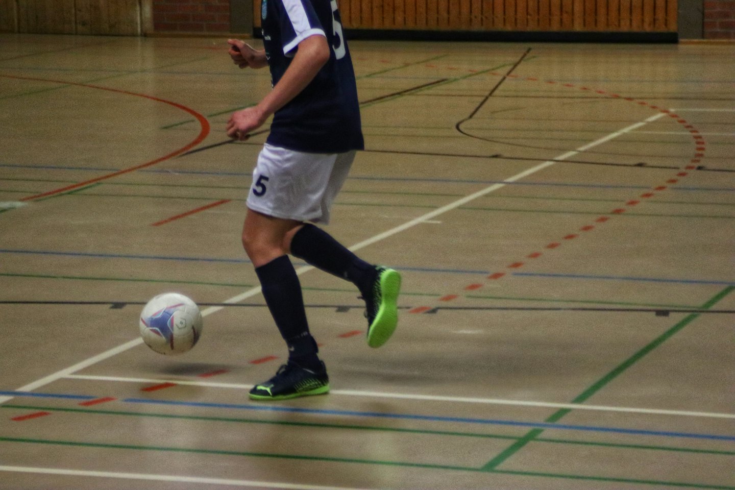 Jugador de fútbol sala regateando un balón en una cancha cubierta.